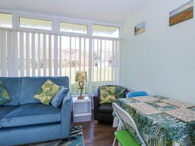 A sitting area with blue sofa and black chair with leaf patterned cushions next to a table with leaf patterned tablecloth at Number 19 in Cromer