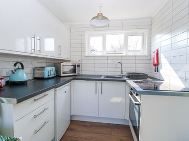 A kitchen with white cabinets black countertops a kettle toaster microwave oven and a window at Number 19 in Cromer