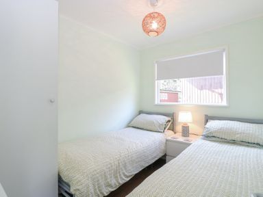 A bedroom with two single beds a nightstand with a lamp and a window with a blind at Number 19 in Cromer