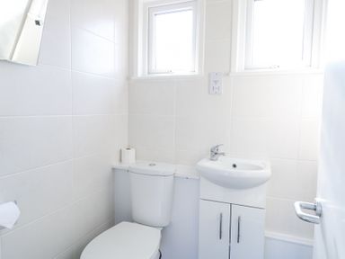 A small bathroom with a toilet and a sink with cabinets under two windows at Number 19 in Cromer