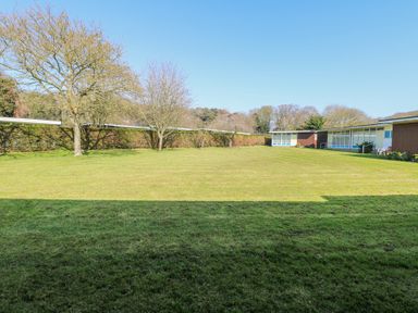A grassy lawn with several leafless trees and modern single-story buildings at Number 19 in Cromer