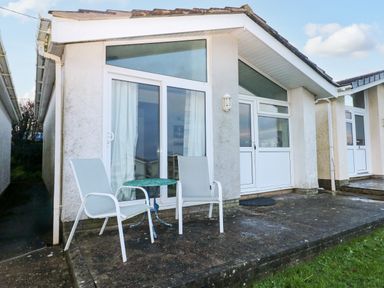 A patio area with two chairs and a small round table outside a bungalow with large windows and a door at Chalet 27 in Port Eynon