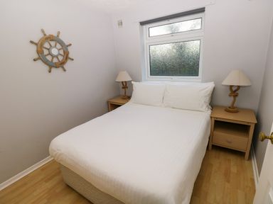 A bedroom with a double bed between two wooden bedside tables with lamps and a window above the bed at Chalet 27 in Port Eynon