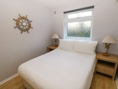 A bedroom with a double bed white bedding bedside tables with lamps and a window at Chalet 27 in Port Eynon
