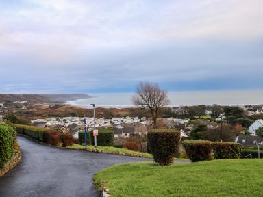 A paved road with hedges and a tree overlooking houses and the sea at Chalet 27 in Port Eynon