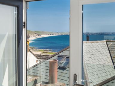 View of a beach and coastline through an open window with rooftops in the foreground at The Loft in Porthleven