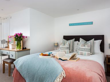 A bedroom with a bed with cushions and an open book on a blanket and a vanity table with flowers at The Loft in Porthleven
