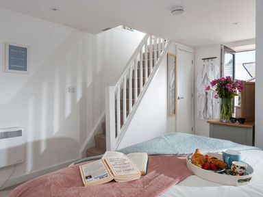 A bedroom with a staircase a tray of breakfast on the bed and flowers on a dresser at The Loft in Porthleven