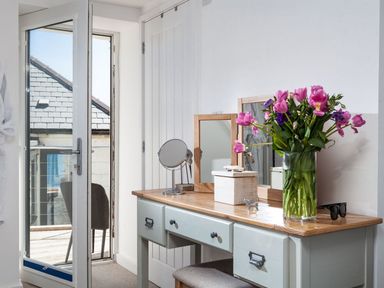 A dressing table with flowers a mirror and accessories next to an open door leading to a balcony at The Loft in Porthleven