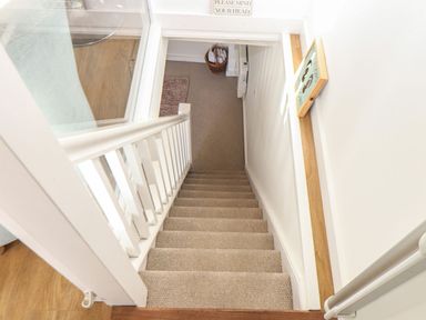 A carpeted staircase with white railings leading down to a small landing with a basket and heater at The Loft in Porthleven
