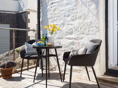 A small outdoor patio with a round table and two chairs with cushions and a basket at The Loft in Porthleven