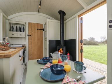 A small kitchen with a wood stove a table set for breakfast and an open door showing grass outside at Hazel South Leigh near Witney