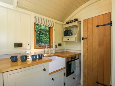 A small kitchen with wooden countertops blue mugs on the counter a white sink and a wooden door at Hazel South Leigh near Witney