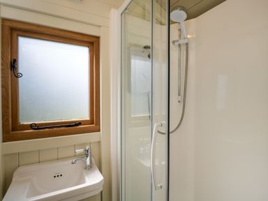 A bathroom with a small sink under a frosted window and a corner shower with a glass door and mounted showerhead at Hazel in South Leigh near Witney