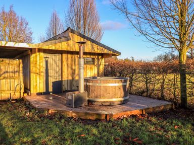 A wooden shed with a hot tub on a concrete platform in a grassy outdoor area at Cedrus Lodge in Skelton near Penrith
