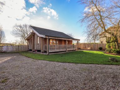 A wooden lodge with a covered porch surrounded by a gravel driveway and a grassy yard at Cedrus Lodge in Skelton near Penrith