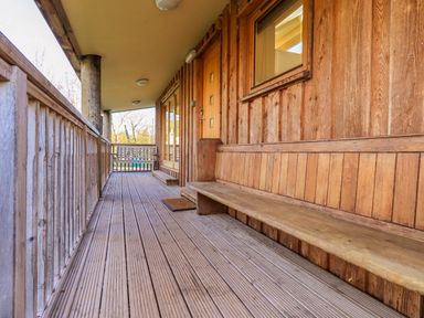 A wooden balcony with built in bench and railing at Cedrus Lodge in Skelton near Penrith