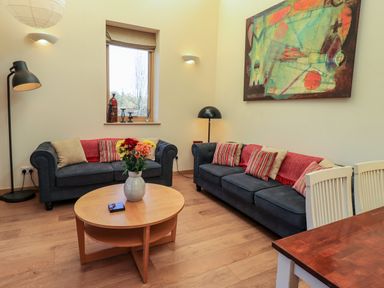 A living room with two blue sofas a round wooden coffee table and a painting on the wall at Cedrus Lodge in Skelton near Penrith