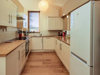 A kitchen with white cabinets wooden countertops a refrigerator stove oven sink and window with blinds at Cedrus Lodge in Skelton near Penrith