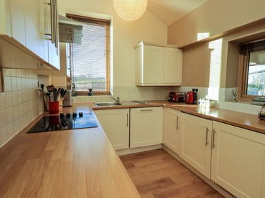 A kitchen with white cabinets wooden countertops a sink a stovetop and small appliances at Cedrus Lodge Skelton near Penrith