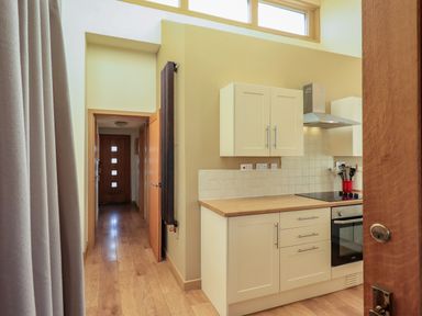 A kitchen with white cabinets wooden countertops and a stove next to a hallway with wooden doors at Cedrus Lodge in Skelton near Penrith