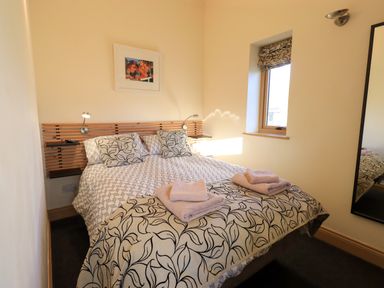 A bedroom with a double bed with patterned bedding and towels on the bed beside a window and a mirror at Cedrus Lodge in Skelton near Penrith