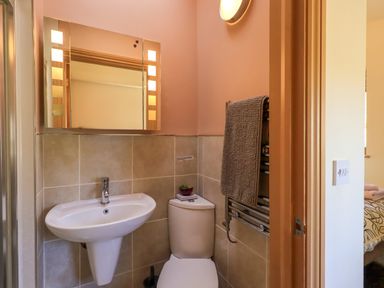 A bathroom with a pedestal sink, toilet, mirror with lights, towel on heated rack at Cedrus Lodge in Skelton near Penrith