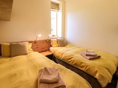 A bedroom with two single beds with yellow bedding and beige towels on top at Cedrus Lodge in Skelton near Penrith