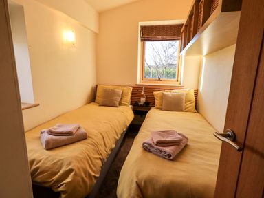 A small bedroom with two single beds with yellow bedding and folded towels on each bed at Cedrus Lodge in Skelton near Penrith