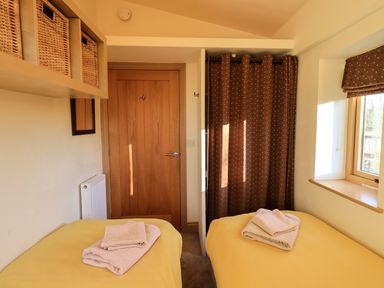 A bedroom with two single beds with towels on them a wooden door and a window with a brown curtain at Cedrus Lodge in Skelton near Penrith