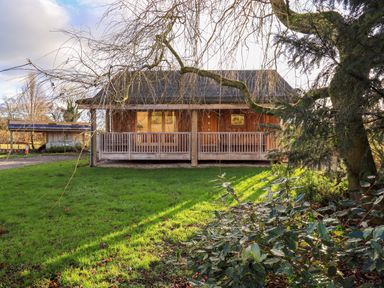 A wooden lodge with a porch railing surrounded by grass and trees at Cedrus Lodge in Skelton near Penrith
