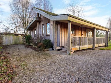 A wooden cabin with a gravel driveway and a porch at Larch Lodge in Skelton near Penrith