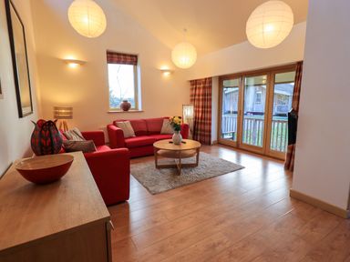A living room with red sofas and a round wooden coffee table at Larch Lodge in Skelton near Penrith