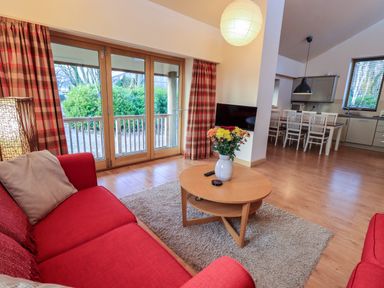 A living room with red sofas a round wooden coffee table with flowers and a TV near dining area at Larch Lodge in Skelton near Penrith