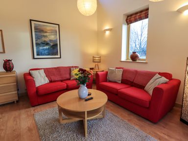 A living room with red sofas a round wooden table a vase with flowers and a window at Larch Lodge in Skelton near Penrith
