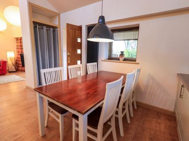 A dining area with a wooden table and six white chairs under a hanging light at Larch Lodge in Skelton near Penrith