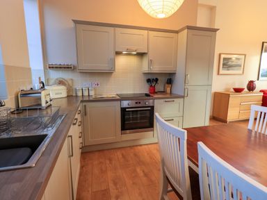 A kitchen with grey cabinets a wooden table with white chairs and a wooden sideboard at Larch Lodge in Skelton near Penrith