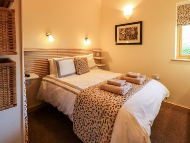 A bedroom with a double bed with patterned bed runner and towels on the bed at Larch Lodge in Skelton near Penrith