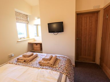 A bedroom with a bed holding towels a wall mounted tv two wooden doors and a window with a patterned blind at Larch Lodge Skelton near Penrith