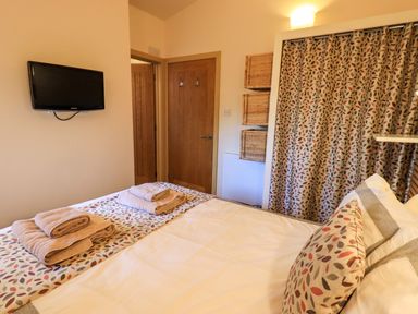 A bedroom with a bed covered with patterned bedding and towels a wall mounted TV wooden doors and patterned curtains at Larch Lodge in Skelton near Penrith
