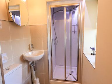 A bathroom with a shower enclosure a wall-mounted sink a toilet and a round mirror at Larch Lodge in Skelton near Penrith