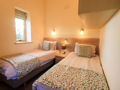 A small bedroom with two single beds a window a nightstand with a lamp and wall lights at Larch Lodge in Skelton near Penrith