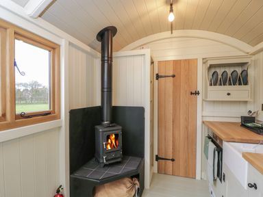 A small kitchen area with a wood burning stove a wooden door and a countertop with a sink at Spindle South Leigh near Witney