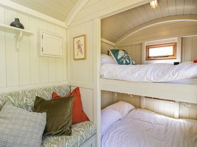 A small bedroom with bunk beds and a cushioned bench seat with pillows at Spindle South Leigh near Witney