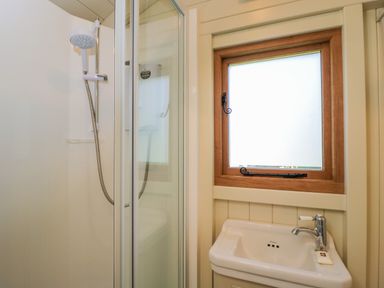 A bathroom with a shower enclosure a handheld showerhead a small sink with a faucet and a frosted window with a wooden frame at Spindle South Leigh near Witney