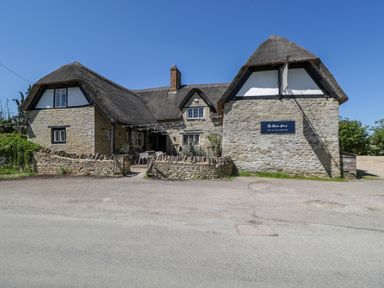 A stone building with thatched roof and outdoor seating behind a low stone wall at Spindle South Leigh near Witney