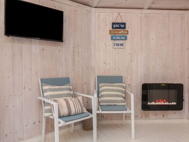 Two chairs with striped cushions a wall-mounted television a wall-mounted electric fireplace and wooden panel walls at Barley Bay near Hartland