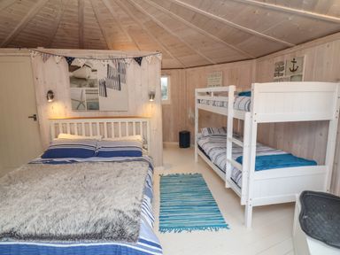 A bedroom with a double bed and bunk beds with blue striped bedding at Barley Bay near Hartland