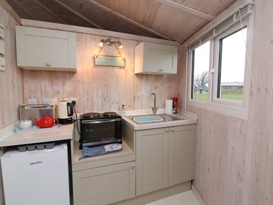 A kitchenette with cabinets a sink a small oven a red kettle and a mini fridge near a window at Barley Bay near Hartland