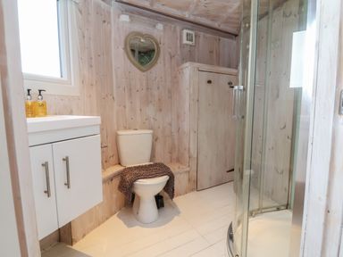 A bathroom with a toilet a shower a white cabinet and a heart shaped mirror at Barley Bay near Hartland